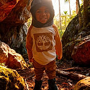 Jamarcus joined the competition — help win amazing prizes! child, smiling, forest, cave, rocks, sunlight, trees, hood, outdoor, nature, person, greenery, daylight, adventure, happy, clothing, boots, young, portrait, environment