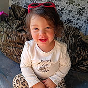 Everleigh is registered to the contest to win money with this photo: armchair, child, clothing, cross_legged, face, floral_wallpaper, happy, home, indoor, leopard_print, long_sleeves, photograph, pink, portrait, sitting, smiling, sunglasses, tiger_stripes, toddler, white_shirt