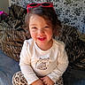 child, toddler, smiling, portrait, sitting, armchair, sunglasses, pink, leopard_print, tiger_stripes, floral_wallpaper, indoor, home, clothing, white_shirt, long_sleeves, cross_legged, happy, face, photograph