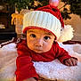 Adriti is registered to the contest to win money with this photo: baby, child, santa_hat, red_clothing, blanket, christmas_tree, ornament, holiday, festive, indoor, cute, portrait, toddler, face, hand, warm_lighting, decorations, seasonal, cozy, expression