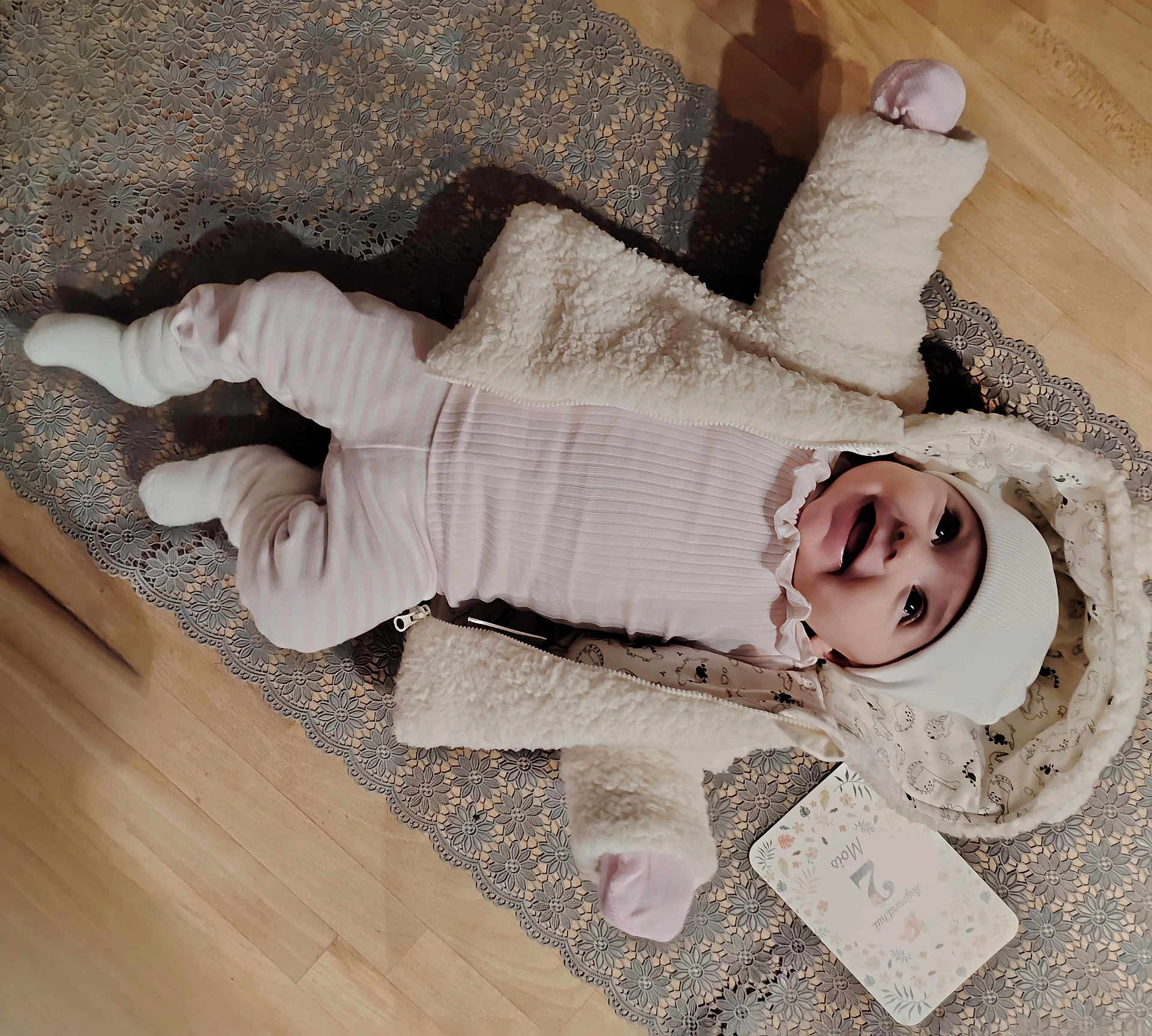 élie a rejoint le concours — aidez-le/la à gagner de superbes lots ! baby, infant, smiling, clothing, hat, jacket, floor, mat, wood, milestone_card, lying_down, happy, cute, child, indoors, warm_clothing, baby_girl, portrait, newborn, soft_texture
