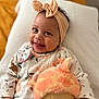 baby, smiling, headband, bow, pacifier, toy, plush, floral_clothing, infant, happy, portrait, child, cute, lying_down, blanket, indoor, soft_toy, face, closeup, person