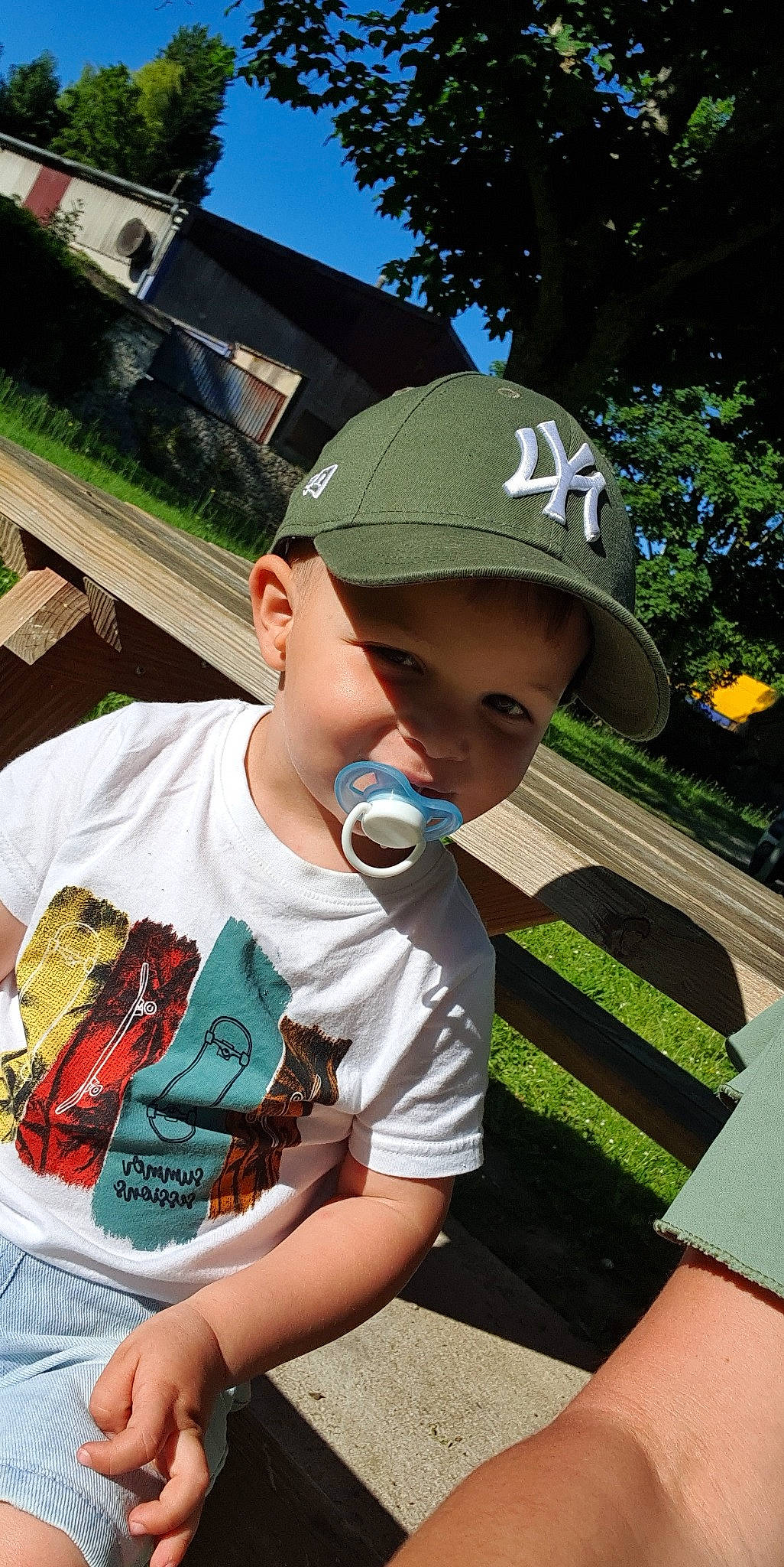 Lenzo participe au concours pour gagner de l'argent avec cette photo : baseball_cap, cap, child, cool, fun, grass, happy, hat, headgear, headwear, leisure, person, plant, public_space, recreation, sitting, sky, summer, t_shirt, toddler