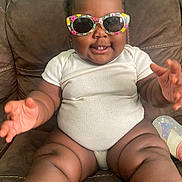 Brazil joined the competition — help win amazing prizes! baby, child, infant, sitting, couch, sunglasses, floral_sunglasses, white_onesie, smiling, happy, portrait, indoor, furniture, bottle, toy, curly_hair, outstretched_hands, bare_feet, close_up, family_photo