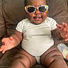 baby, child, infant, sitting, couch, sunglasses, floral_sunglasses, white_onesie, smiling, happy, portrait, indoor, furniture, bottle, toy, curly_hair, outstretched_hands, bare_feet, close_up, family_photo
