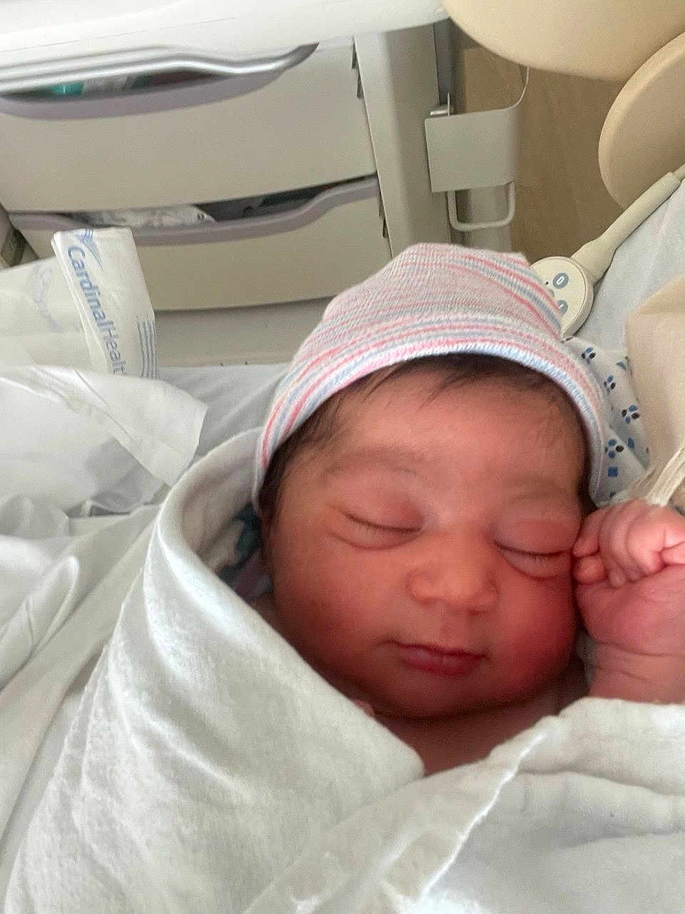 Elian is registered to the contest to win money with this photo: newborn, baby, sleeping, hospital, blanket, hat, infant, bed, medical_equipment, bassinet, face, peaceful, wrapped, person, cute, closeup, skin, indoors, healthcare, resting