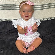 Lottie. B is registered to the contest to win money with this photo: baby, child, smiling, clapping, sitting, headband, bow, white_shirt, pink_clothing, barefoot, couch, blanket, indoor, happy, cute, infant, portrait, person, furniture, home