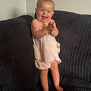 Lottie M B joined the competition — help win amazing prizes! baby, child, smiling, clapping, standing, couch, dark_fabric, pink_clothing, happy, indoors, person, infant, cute, portrait, barefoot, texture, home, furniture, light, expression
