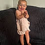 baby, child, smiling, clapping, standing, couch, dark_fabric, pink_clothing, happy, indoors, person, infant, cute, portrait, barefoot, texture, home, furniture, light, expression