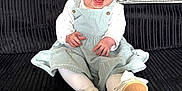 Lottie is registered to the contest to win money with this photo: baby, child, smiling, sitting, headband, dress, white_shoes, bow, tights, couch, black_couch, corduroy, happy, infant, indoors, cute, portrait, person, fashion, joyful