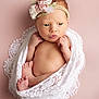 newborn, baby, infant, wrapped, lace_blanket, headband, flowers, pink_background, cute, tiny_feet, hands_near_face, portrait, soft_lighting, indoors, child, skin, expression, closeup, sleepy, adorable
