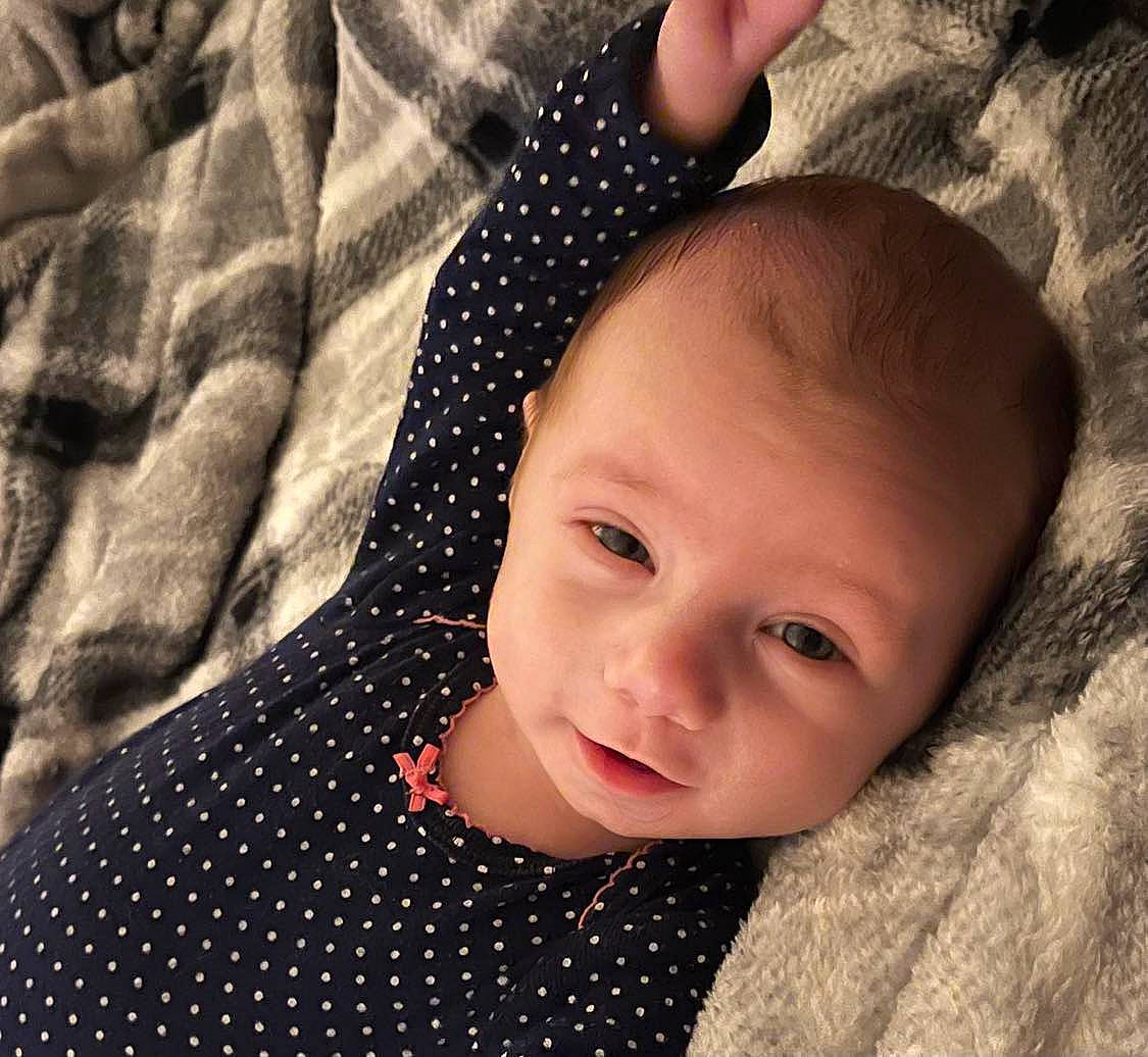 Esme is registered to the contest to win money with this photo: baby, baby_toddler_clothing, black, cheek, child, comfort, eyelash, flash_photography, gesture, happy, iris, lip, nose, pattern, person, skin, sleeve, smile, textile, toddler