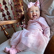 Aubrey is registered to the contest to win money with this photo: baby, infant, smiling, headband, pink_dress, tutu, socks, rocking_chair, wooden_spindle, garland, decorations, blanket, cushion, portrait, indoor, happy, tongue_out, cute, soft_lighting, celebration