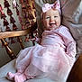 baby, infant, smiling, headband, pink_dress, tutu, socks, rocking_chair, wooden_spindle, garland, decorations, blanket, cushion, portrait, indoor, happy, tongue_out, cute, soft_lighting, celebration