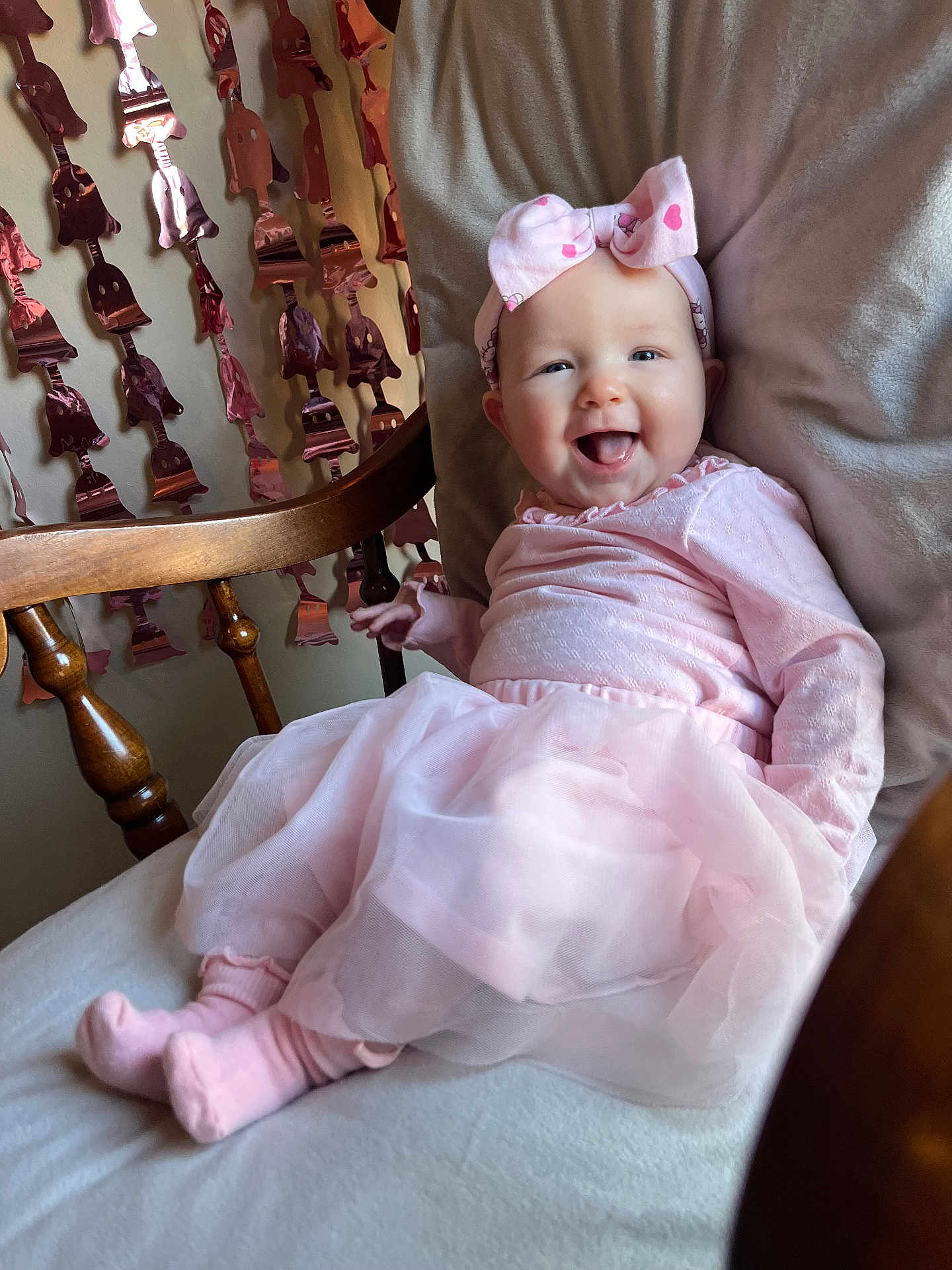 Aubrey is registered to the contest to win money with this photo: baby, infant, smiling, headband, pink_dress, tutu, socks, rocking_chair, wooden_spindle, garland, decorations, blanket, cushion, portrait, indoor, happy, tongue_out, cute, soft_lighting, celebration