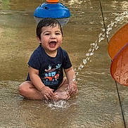 Jose Jr joined the competition — help win amazing prizes! toddler, child, water_play, splashing, smiling, wet_hair, navy_shirt, outdoor, playground, water_spray, concrete, fun, happy, sitting, summer, cute, boy, water_park, joy, play