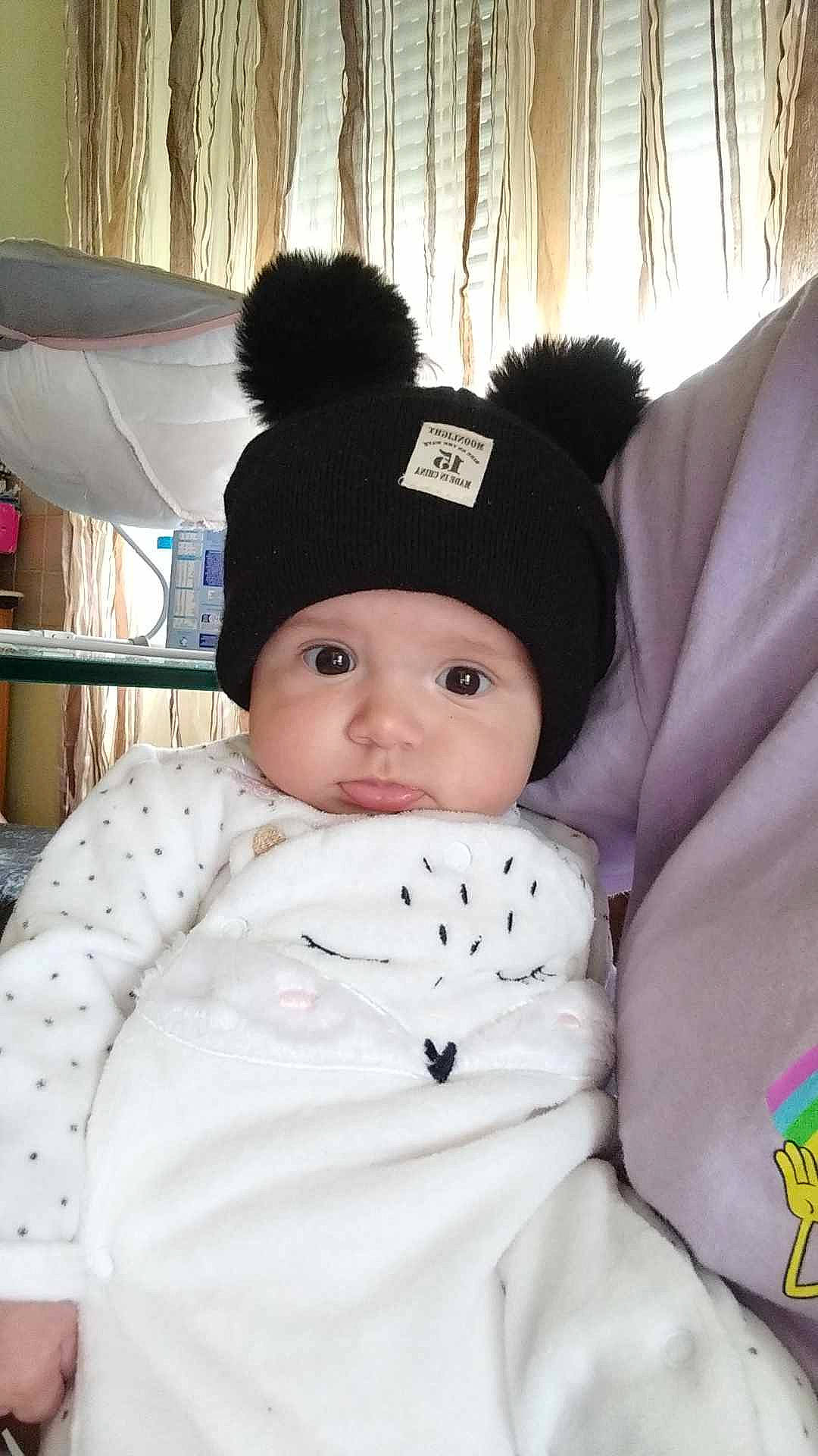 Djenessy a rejoint le concours — aidez-le/la à gagner de superbes lots ! baby, baby_toddler_clothing, beanie, cap, cheek, child, comfort, eye, fun, fur, happy, head, headwear, linens, pattern, person, room, sitting, skin, sleeve