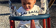 Milaní joined the competition — help win amazing prizes! toddler, child, swing, playground, outdoor, smiling, happy, person, clothing, white_outfit, fence, grass, sunlight, tongue_out, hair_bun, metal_chain, play, fun, daytime, park
