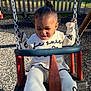 toddler, child, swing, playground, outdoor, smiling, happy, person, clothing, white_outfit, fence, grass, sunlight, tongue_out, hair_bun, metal_chain, play, fun, daytime, park