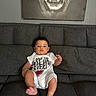 Mason is registered to the contest to win money with this photo: baby, child, infant, couch, sofa, living_room, onesie, clothing, face, person, painting, tiger, wall, home, furniture, seated, cute, indoor, expression, relaxed