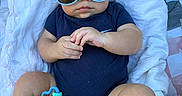 Mason is registered to the contest to win money with this photo: baby, sunglasses, toy, blanket, outdoor, grass, blue_onesie, infant, cute, child, person, legs, hands, face, fashion, relaxing, summer, playful, accessory, cool