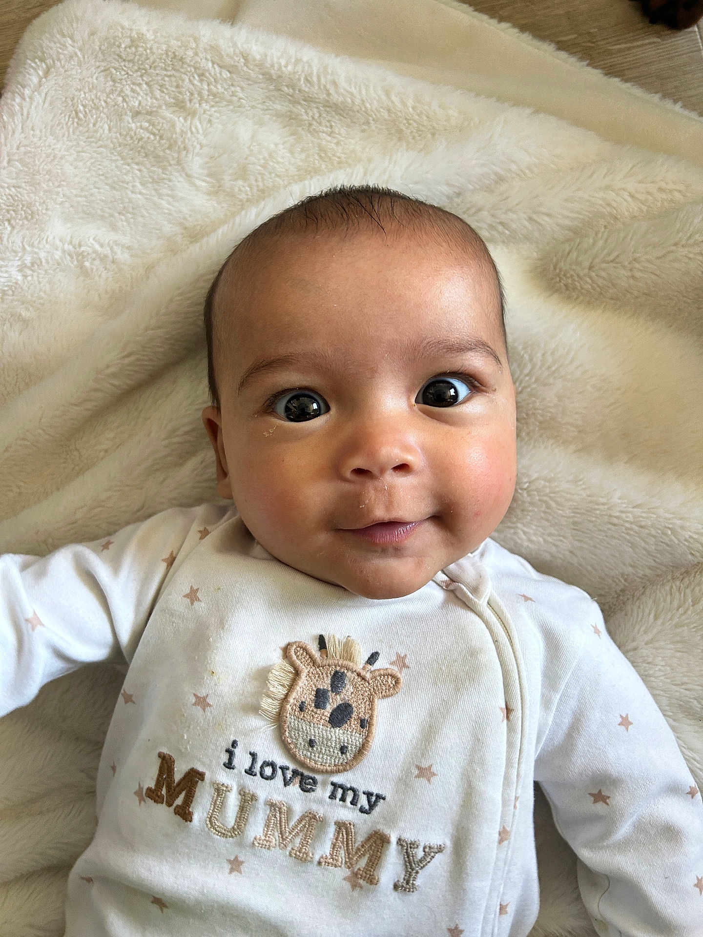 Pippin is registered to the contest to win money with this photo: adorable, baby, blanket, child, closeup, cozy, cute, eyes, face, giraffe_embroidery, happy, indoor, infant, lying_down, newborn, portrait, smile, soft_texture, warm, white_clothing
