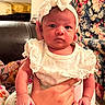 baby, bow, child, couch, cute, expression, face, floral_pattern, furniture, hand, headband, holding, indoor, infant, person, portrait, seated, skin, white_clothing, young