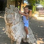 bench, child, clothing, curiosity, daytime, exploration, gravel, lion, nature, outdoor, park, play, sandals, sculpture, shadow, statue, summer, sunlight, trees, young