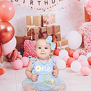 Kyra is registered to the contest to win money with this photo: baby, balloons, birthday, blue, bow, celebration, child, cute, decorations, dress, floor, gift, happy, headband, one, party, pink, presents, smile, white