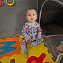 baby, child, pajamas, foam_mat, playpen, indoor, colorful, sitting, floor, toy, curious, puzzle_mat, footwear, patterned_clothing, young_child, infant, looking_up, bright_colors, home, play_area