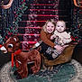 child, baby, smiling, sleigh, plush_toy, reindeer, christmas, holiday, decorations, tree, gift, stairs, carpet, wood_floor, indoor, portrait, happy, festive, family, cute