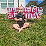 baby, child, grass, outdoor, birthday, sign, happy_birthday, moawk, sunny, daylight, house, window, flower, greenery, celebration, one_year_old, infant, portrait, sitting, cute