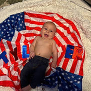 Tyler joined the competition — help win amazing prizes! baby, infant, smiling, american_flag, blanket, fluffy_rug, child, happy, portrait, indoors, colorful_letters, clothing, bare_chest, jeans, cute, lying_down, decor, soft_texture, celebration, patriotic