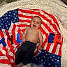 baby, infant, smiling, american_flag, blanket, fluffy_rug, child, happy, portrait, indoors, colorful_letters, clothing, bare_chest, jeans, cute, lying_down, decor, soft_texture, celebration, patriotic