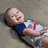Tyler is registered to the contest to win money with this photo: baby, carpet, child, clothing, colorful, expression, face, hand, infant, lying_down, onesie, playful, reaching, smiling, toy, toys, young_child, indoor, person, happy
