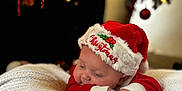 Jayden is registered to the contest to win money with this photo: baby, christmas_hat, red_clothing, white_blanket, sleeping, holiday, festive, face, infant, cute, holiday_decor, christmas_tree, ornaments, soft_lighting, cozy, closeup, celebration, holidays, child, resting