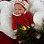 baby, christmas, holiday, red_clothing, santa_hat, blanket, decorations, christmas_tree, lights, festive, cute, infant, indoors, holiday_season, cozy, smiling, face, headwear, celebration, soft_texture