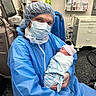Aryanna Lott joined the competition — help win amazing prizes! newborn, baby, infant, medical_worker, healthcare, hospital, scrubs, surgical_mask, hairnet, protective_gown, cradling, blanket, pink_hat, swaddled, operating_room, medical_equipment, hospital_bed, chair, portrait, caregiving