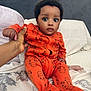 baby, infant, child, onesie, orange_clothing, bed, hand, person, cute, wide_eyes, animal_print, sitting, indoor, portrait, soft_lighting, calm_expression, bedroom, pillow, blanket, cozy
