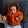 Zimuzochukwu joined the competition — help win amazing prizes! baby, child, hooded_jacket, orange_clothing, blue_pants, curly_hair, indoor, couch, pillow, knit_blanket, fist, wide_eyes, cute, portrait, seated, infant, warm_clothing, cozy, expression, person