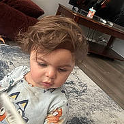 Jenna is registered to the contest to win money with this photo: toddler, child, indoor, carpet, toy, book, hair, face, clothing, living_room, furniture, table, television, sippy_cup, person, floor, curious, cute, casual, home