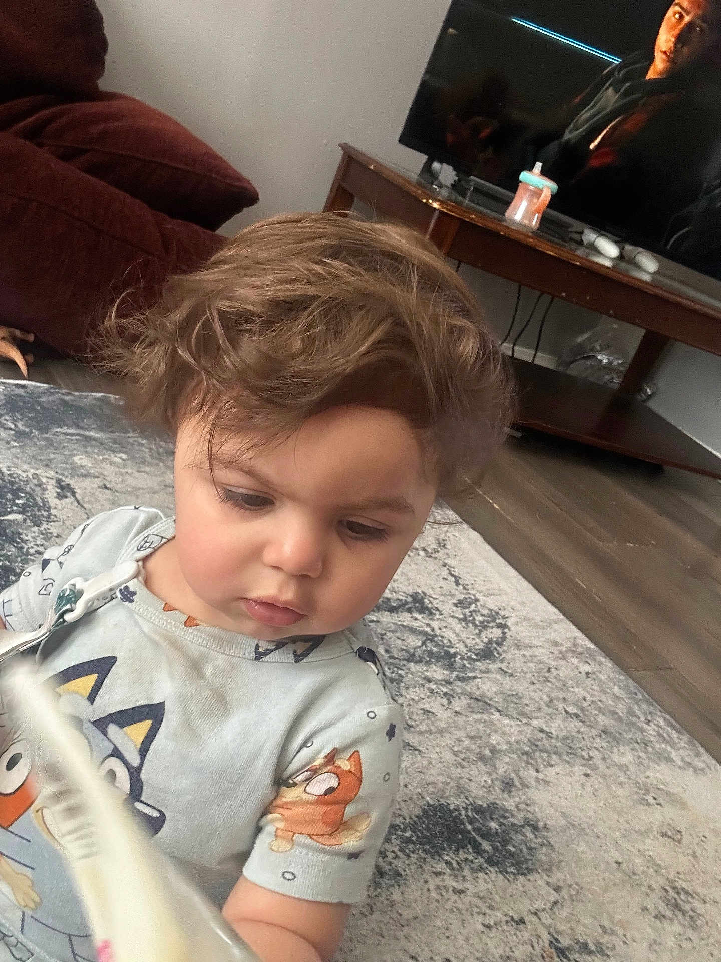 Jenna is registered to the contest to win money with this photo: toddler, child, indoor, carpet, toy, book, hair, face, clothing, living_room, furniture, table, television, sippy_cup, person, floor, curious, cute, casual, home