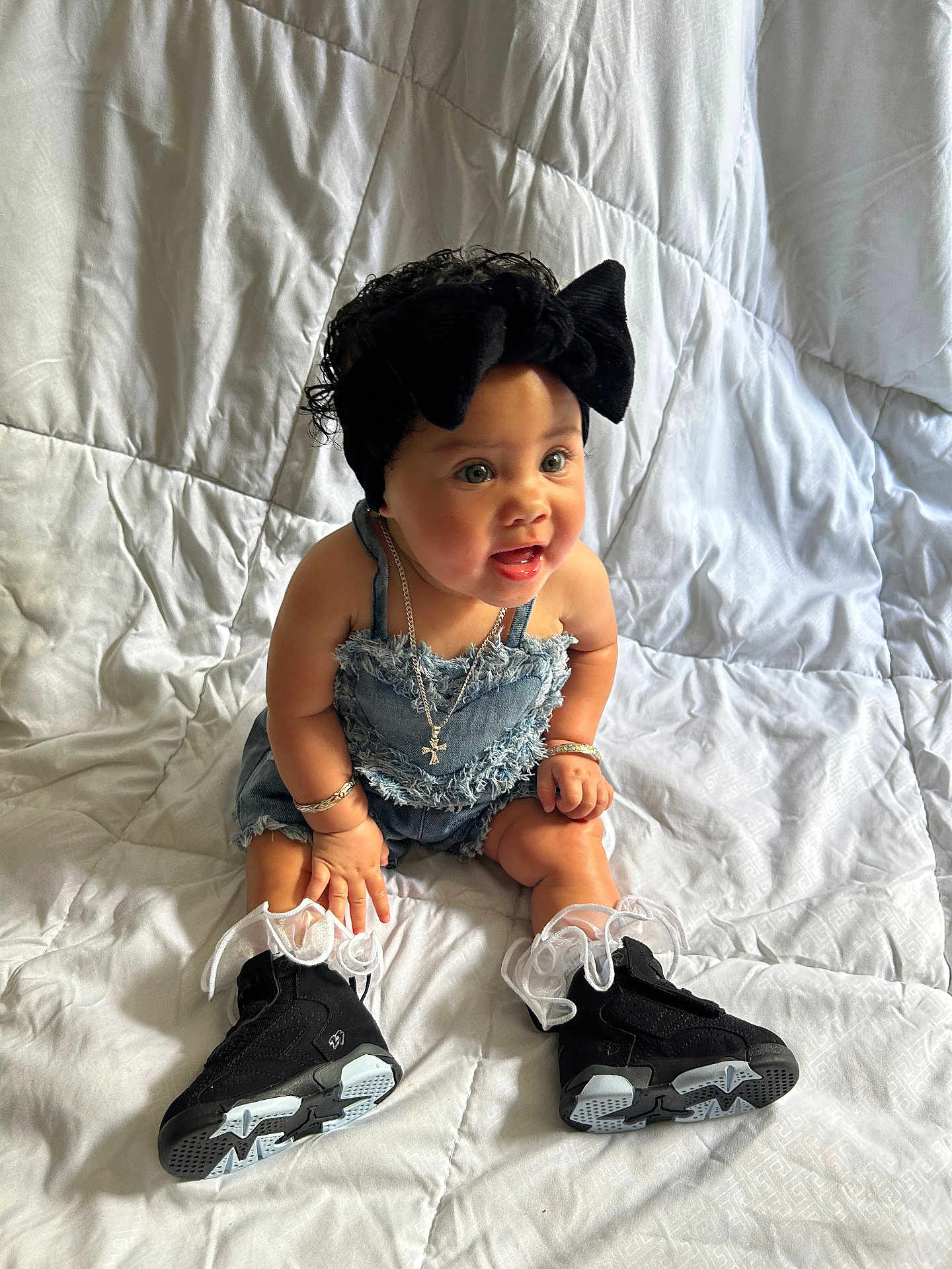 Hermoni is registered to the contest to win money with this photo: baby, child, denim_outfit, black_sneakers, headband, bow, jewelry, bracelet, necklace, white_quilt, sitting, smiling, cute, indoor, portrait, curly_hair, happy, infant, fashion, accessories