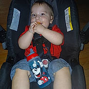 Dominic joined the competition — help win amazing prizes! baby, child, car_seat, sippy_cup, mickey_mouse, snack, red_shirt, denim_shorts, face, hands, legs, floor, seat_belt, indoor, person, smiling, cute, happy, infant, food