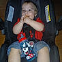 baby, child, car_seat, sippy_cup, mickey_mouse, snack, red_shirt, denim_shorts, face, hands, legs, floor, seat_belt, indoor, person, smiling, cute, happy, infant, food