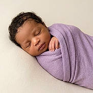 Zoey is registered to the contest to win money with this photo: newborn, baby, sleeping, portrait, swaddled, lavender_wrap, infant, peaceful, cozy, close_up, face, curly_hair, closed_eyes, hand, blanket, soft_lighting, cream_background, indoors, photography, resting