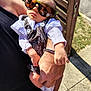 baby, sunglasses, person, hand, arm, clothing, outdoor, sunlight, shadow, skin, bracelet, foot, toe, fabric, pattern, bench, pavement, relaxation, reflection, casual