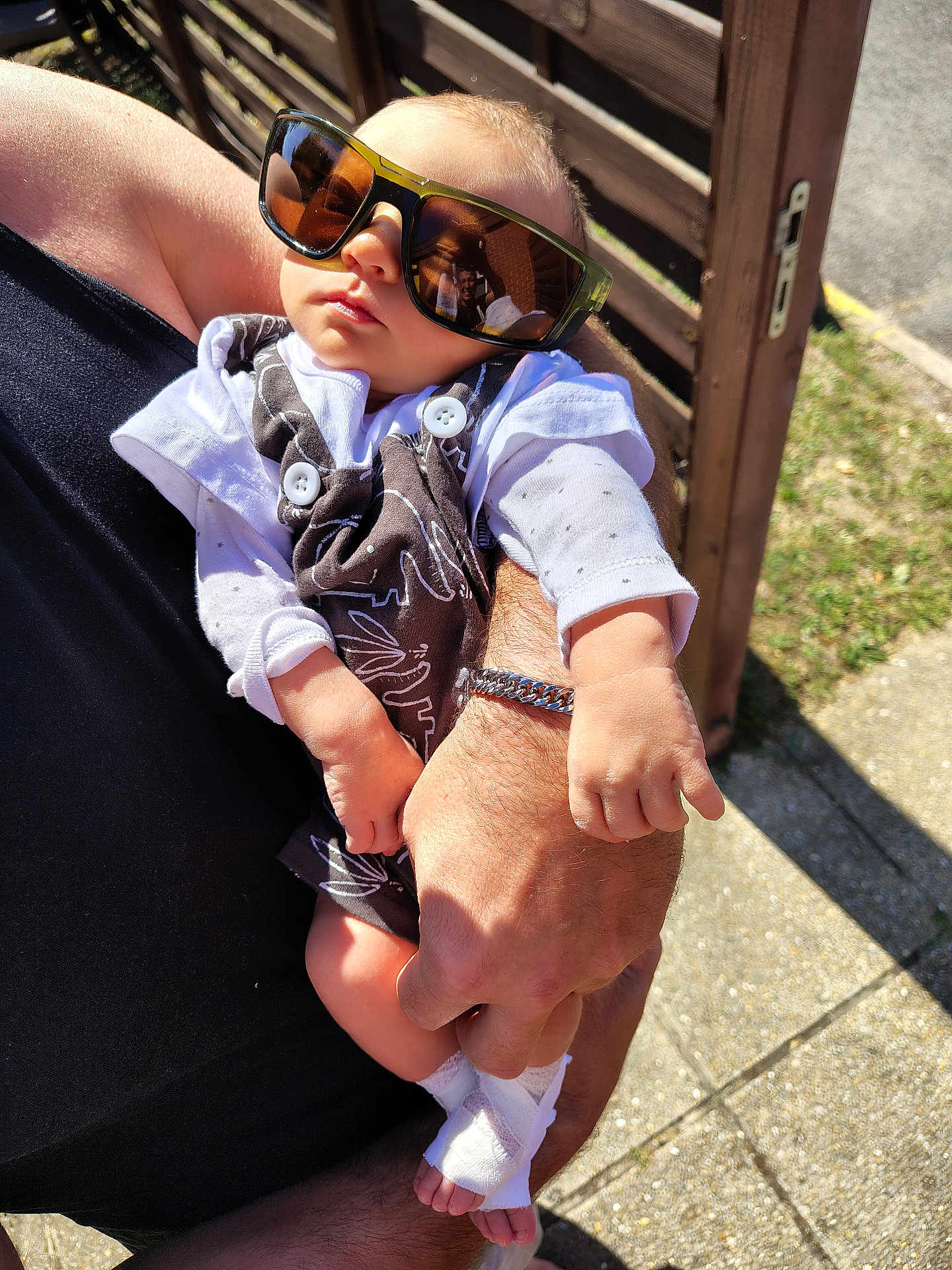 Thélyo participe au concours pour gagner de l'argent avec cette photo : baby, sunglasses, person, hand, arm, clothing, outdoor, sunlight, shadow, skin, bracelet, foot, toe, fabric, pattern, bench, pavement, relaxation, reflection, casual