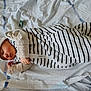 baby, sleeping, bed, striped_swaddle, hat, pacifier, hand, blanket, infant, cute, resting, cozy, indoors, child, newborn, face, clothing, soft, peaceful, toddler