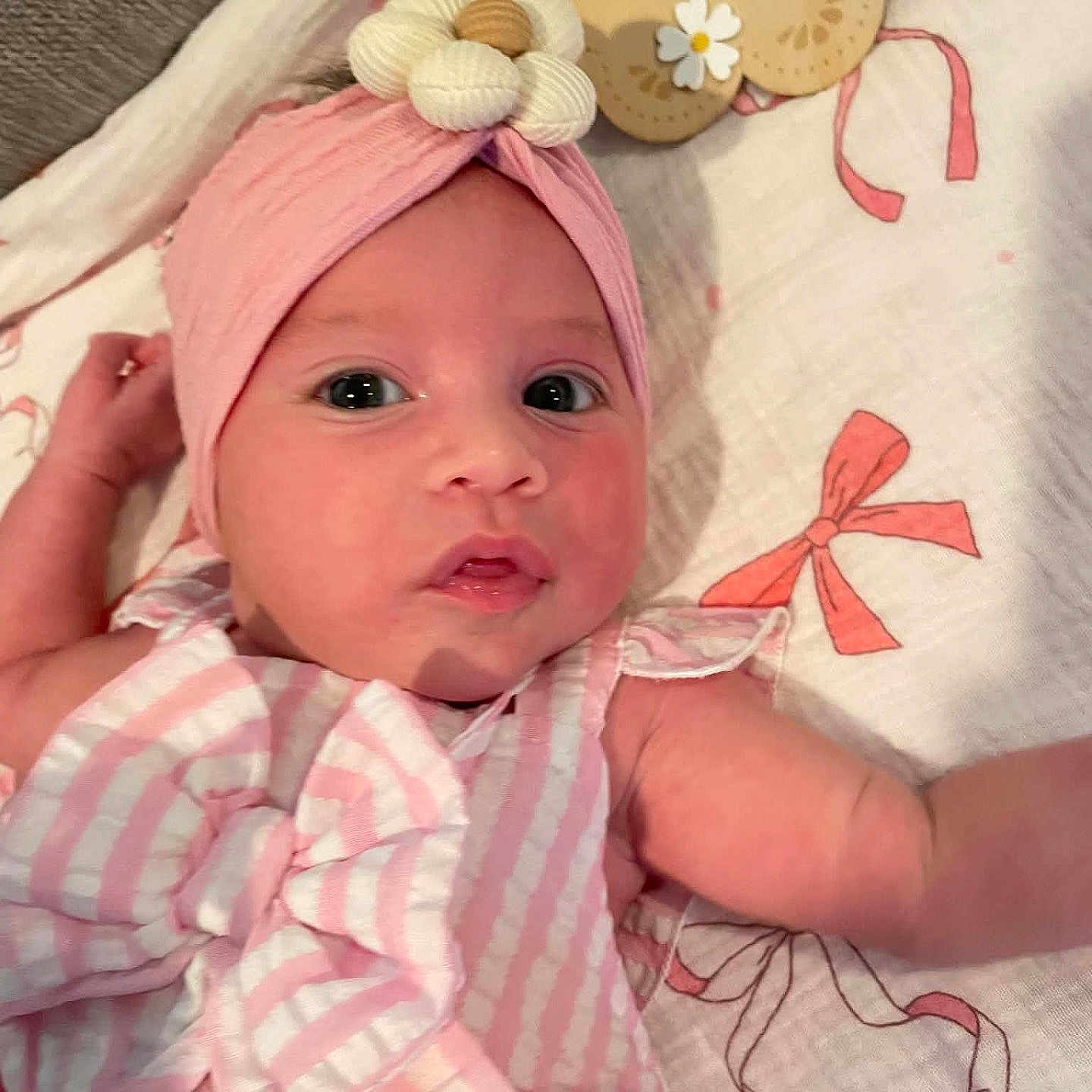 Michaela Rayne joined the competition — help win amazing prizes! baby, bedding, blanket, child, close_up, cute, eyes, face, flower, headband, indoor, infant, looking_at_camera, lying_down, name_sign, photography, pink_outfit, portrait, striped_clothing, wide_eyed
